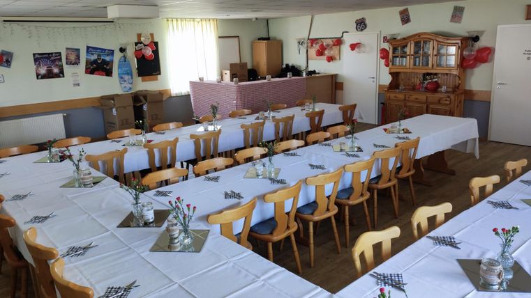 A large room with two long tables covered with white tablecloths. In the background, there is a bar and decorative wall paintings.