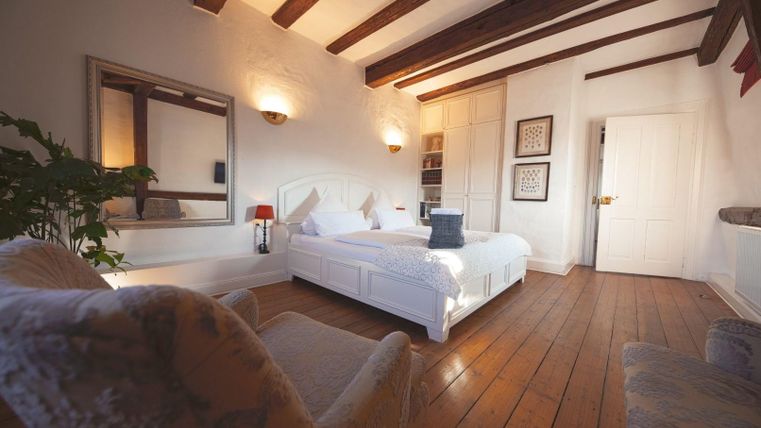 A cozy bedroom with a double bed and wooden beam ceiling. The room has large windows and stylish furniture.