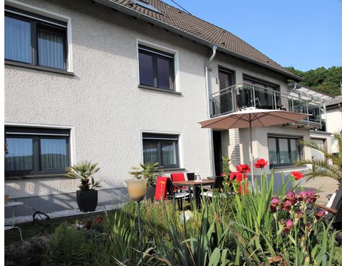 Ein schönes Haus mit einem Balkon und einem einladenden Garten. Bunte Blumen und ein Tisch mit Stühlen laden zum Entspannen ein.