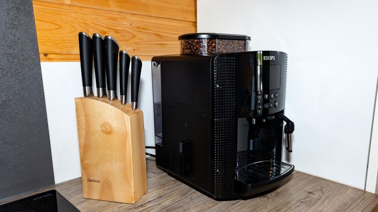 A modern coffee machine is placed on a kitchen counter next to a knife block with razor-sharp kitchen knives. The wooden block gives the kitchen a warm ambiance.