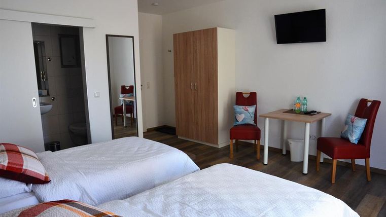Ein modernes Zimmer mit zwei Einzelbetten, einem Tisch und zwei Stühlen. An der Wand hängt ein Fernseher, und es gibt einen Spiegel sowie einen Kleiderschrank.