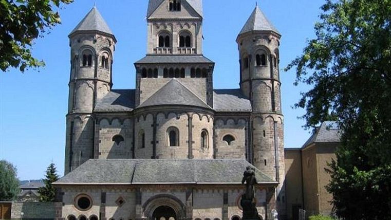 Eine beeindruckende Kirche mit mehreren Türmen und einem charakteristischen Dach. Umgeben von grünem Gras und Bäumen.