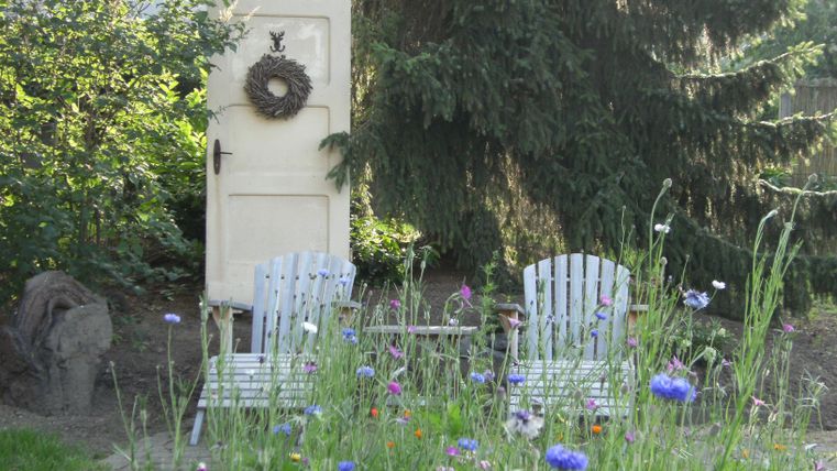 Ein schöner Garten mit zwei Stühlen und einer alten Tür im Hintergrund. Die Wiese ist mit bunten Blumen bewachsen.