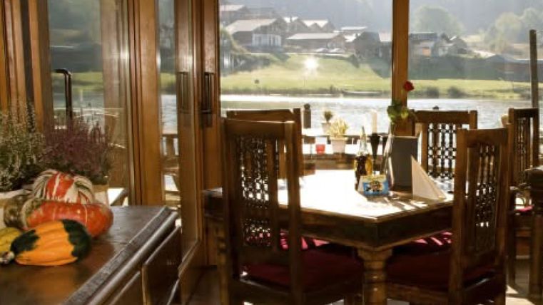 Ein gemütliches Restaurant mit Holztischen und Stühlen. Die großen Fenster bieten einen schönen Blick auf die Landschaft.