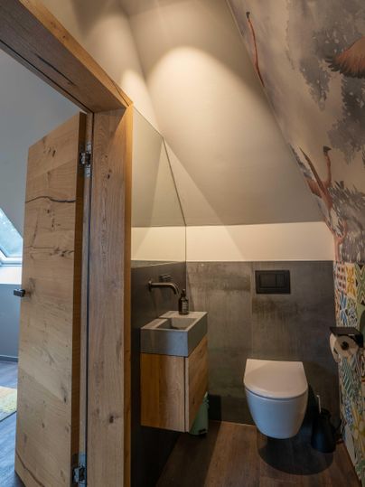 Ein modernes Badezimmer mit Holz- und Betonelementen. An der Wand ist eine farbenfrohe Tapete mit Naturmotiven zu sehen.