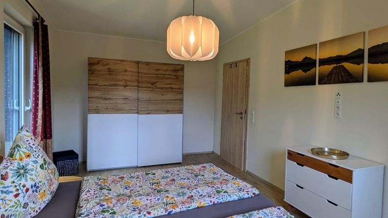 Ein gemütliches Schlafzimmer mit zwei Betten und bunten Blumenmustern. Es gibt einen modernen Kleiderschrank, eine Kommode und ein Fenster mit Vorhängen.