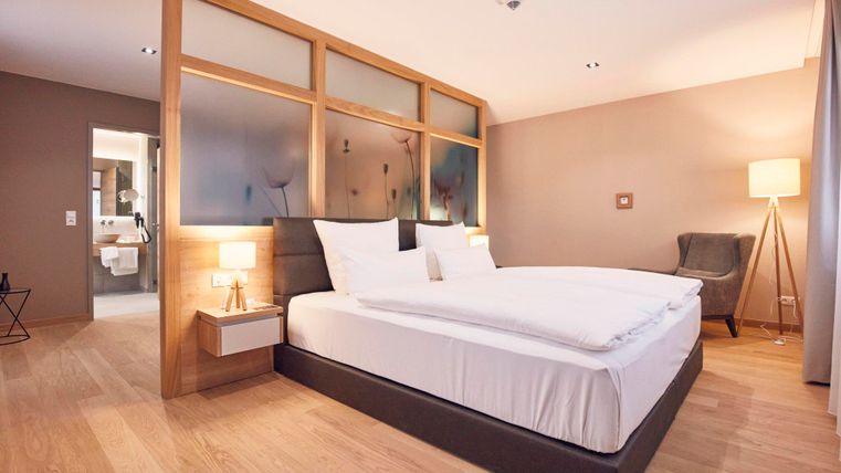 Ein modernes Schlafzimmer mit einem großen Doppelbett und eleganten Nachttischen. Die warme Farbgestaltung und das Holzparkett schaffen eine gemütliche Atmosphäre.