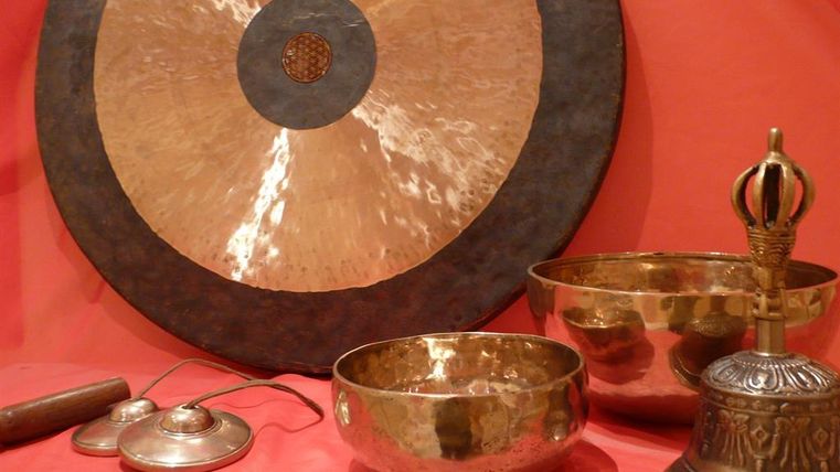 A set of various musical instruments, including a large gong, several bowls, and a xylophone. The objects are arranged on a red-orange background.