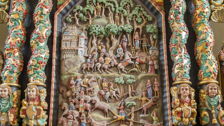 Ein kunstvolles Relief zeigt eine bunte Szene mit Rittern und Bäumen. Im Hintergrund ist ein Schloss und zahlreiche Figuren dargestellt.