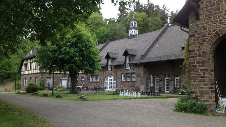 Ein historisches Gebäude aus Stein mit einem grünen Garten und Bäumen. Der Weg führt direkt zu dem charmanten Gebäude im ländlichen Umfeld.