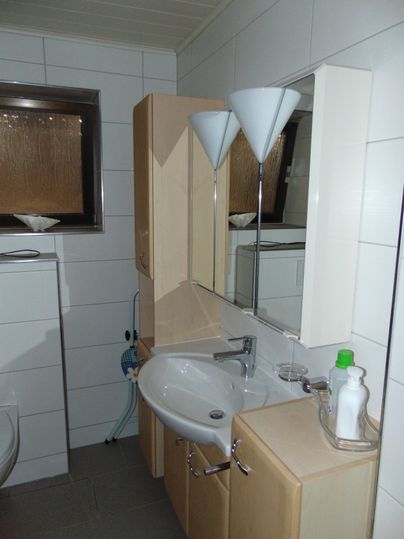A modern bathroom with a bright tiled floor and wooden cabinets. The sink area is clean and well organized.