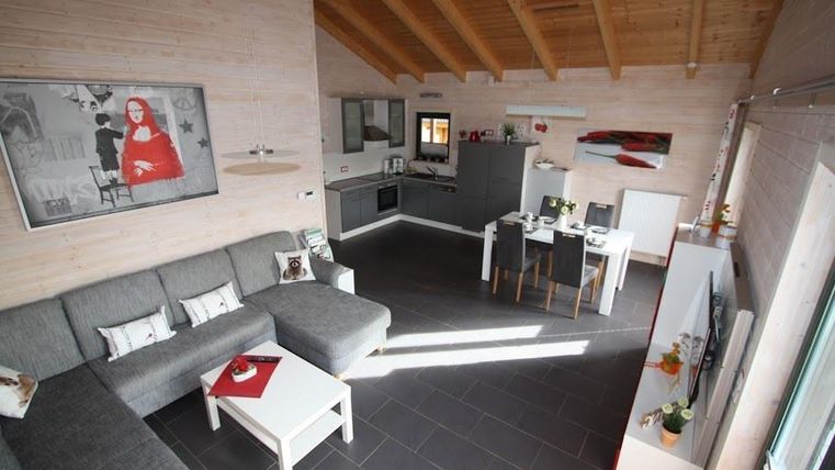 Ein modernes Wohnzimmer mit einer großen grauen Couch und einem weißen Tisch. Die Wände sind aus Holz, und die Küche ist offen und gut ausgestattet.