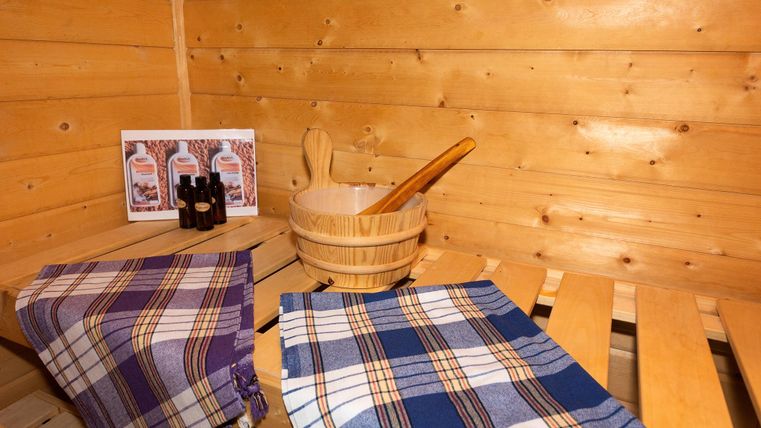 A cozy sauna with wooden paneling. In the foreground are two towels and a wooden container with a ladle.