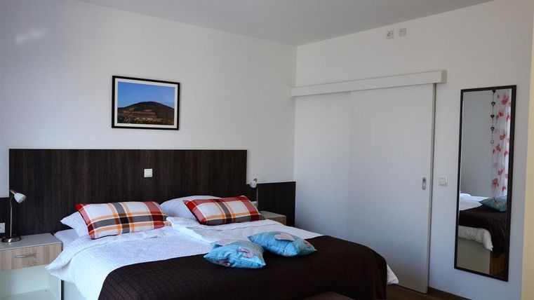 Ein modernes Schlafzimmer mit zwei Betten und bunten Kissen. An der Wand hängen ein Bild und ein Spiegel, und der Raum wirkt hell und freundlich.