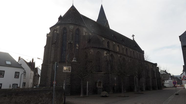 A historic building with a distinctive spire and many windows. The facade is made of dark stone and the sky is overcast.