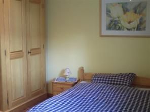 A cozy bedroom with a wooden box and a bed with checked bedding. A picture of flowers is hanging on the wall.
