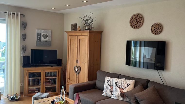 Ein gemütliches Wohnzimmer mit einer grauen Couch und einem Holztisch. Die Wände sind dekoriert und ein Fernseher hängt an der Wand.