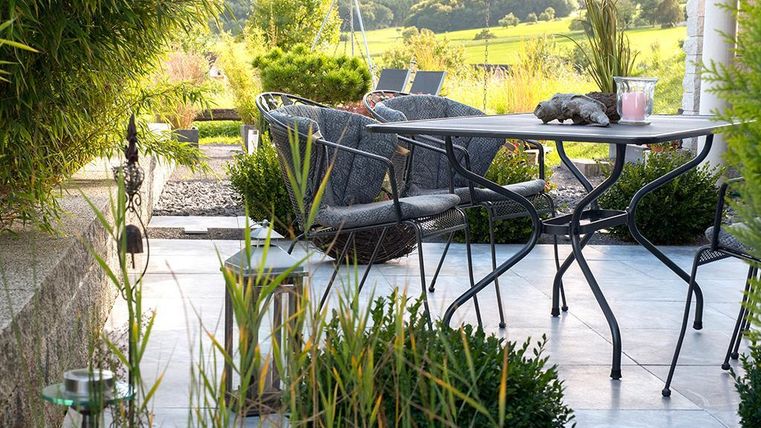 Ein gemütlicher Außenbereich mit einem Tisch und Stühlen aus Rattan. Umgeben von grünen Pflanzen und einer ruhigen, natürlichen Landschaft.