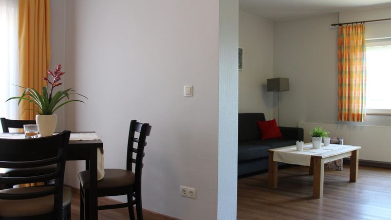 Ein gemütlicher Wohnbereich mit einem Sofa und einem Tisch. Auf der anderen Seite befindet sich ein Essbereich mit Stühlen und einer Pflanze.