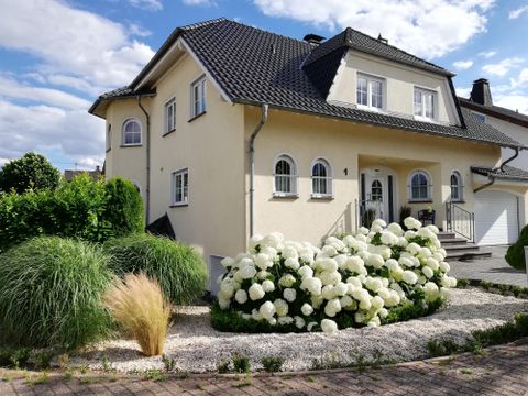 Ein hübsches Haus mit einer hellen Fassade und einem schwarzen Dach. Der Garten ist mit großen, weißen Blumen und grünem Gras gestaltet.