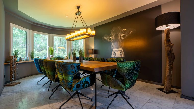 Ein stilvoller Essbereich mit einem großen Tisch und bunten Stühlen. Eine moderne Lampe und Pflanzen sorgen für eine einladende Atmosphäre.