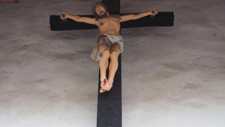 Ein Kruzifix mit einer Darstellung von Jesus, der am Kreuz hängt. Der Hintergrund ist schlicht und neutral.