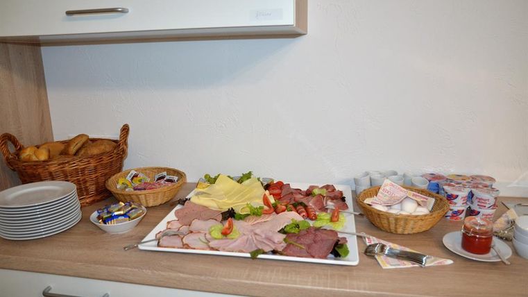 Ein Buffet mit verschiedenen Wurst- und Käsesorten auf einem weißen Teller. Daneben liegt frisches Brot und diverse Aufstriche in Körben.
