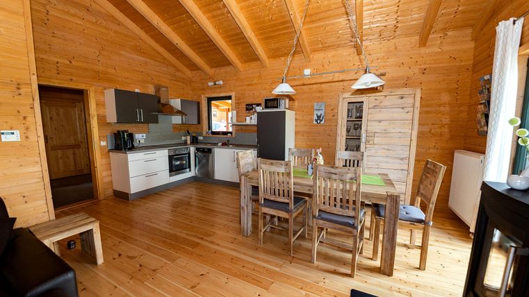 A cozy wooden apartment with an open kitchen and dining area. Bright walls and rustic furniture create a warm atmosphere.