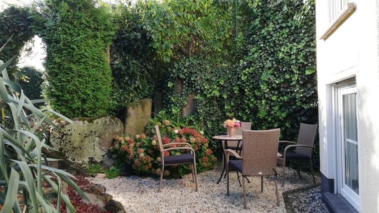 A cozy garden area with chairs and a table. Surrounded by green plants and hedges.