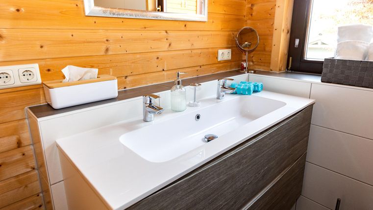 A modern bathroom with an elegant wooden vanity. The walls are made of wood, and the decor feels bright and inviting.