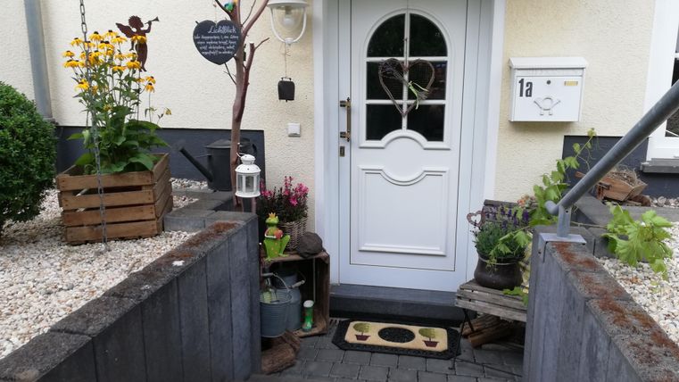 An inviting front door with a beautiful staircase and plants. Next to the door is a small lantern and a welcome mat.