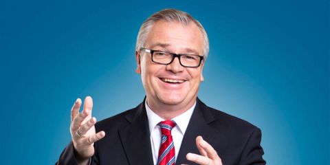 A smiling man in a suit with a tie. The background is blue and conveys a friendly atmosphere.