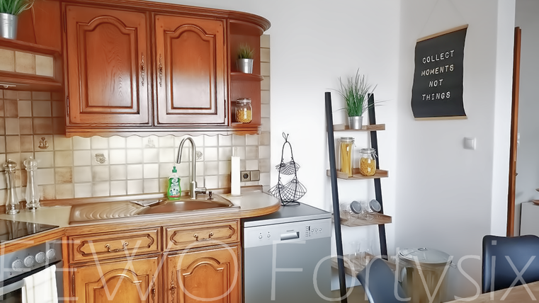 A cozy kitchen with wooden cabinets and modern appliances. In the background, there are plants and decorative elements.