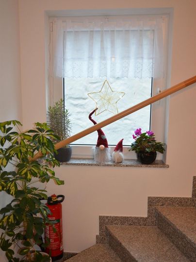Ein gemütlicher Treppenaufgang mit einem Fenster. Auf der Fensterbank stehen Pflanzen, Weihnachtsdekoration und eine Feuerwehrspritze.