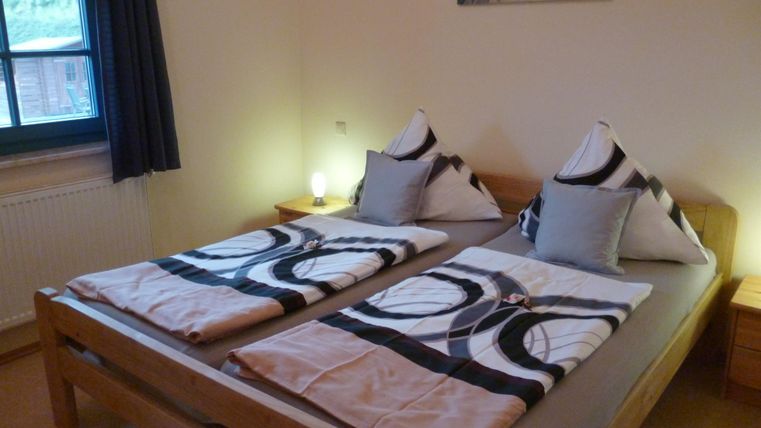 A cozy bedroom with two single beds and modern bedding. The walls are painted in neutral colors, and a window provides daylight.