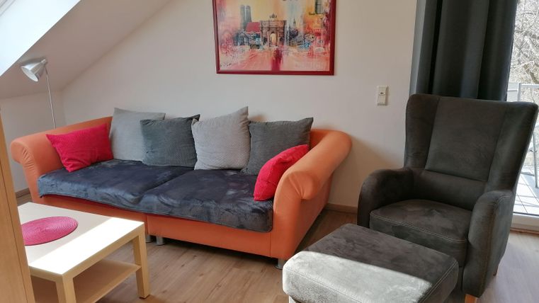 A cozy living room with an orange sofa and a gray armchair. A colorful picture hangs on the wall and there is a small table.