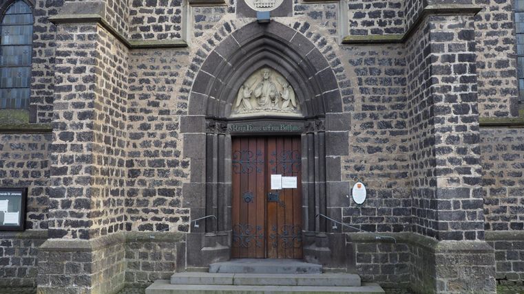 An impressive wooden church door, surrounded by a stone wall. The entrance portal displays architectural details and a serene atmosphere.
