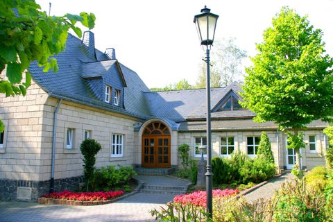 Ein schönes Haus mit einem gepflegten Garten und vielen grünen Bäumen. Die Eingangstür ist einladend und die Umgebung strahlt Ruhe aus.