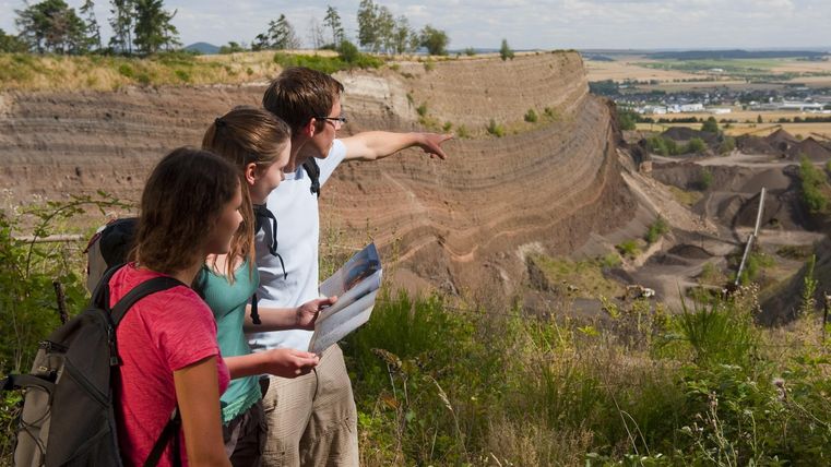 A group of people is standing on a slope and looking at a rocky landscape. They are holding a map and discussing as they explore the surroundings.