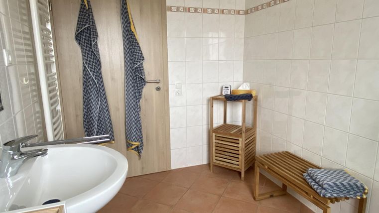 Ein modernes Badezimmer mit einem Waschbecken, einem Holzregal und zwei Handtüchern. Die Wände sind gefliest und die Einrichtung ist hell und einladend.