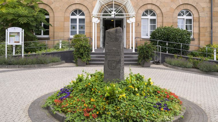 Ein schönes Hotel mit einer einladenden Fassade und einem blühenden Blumenbeet im Vordergrund. Der Eingang ist von Bäumen umgeben, was eine friedliche Atmosphäre schafft.