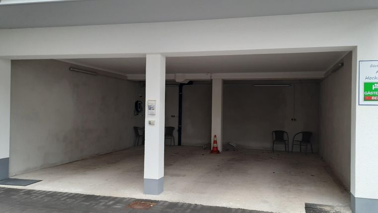 Eine leere Garage mit weiße Wänden und einem grauen Boden. Es sind einige Stühle vorhanden und ein Schild an der Wand.