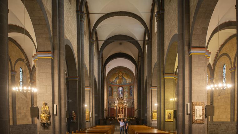 Eine wunderschöne Kirche mit hohen Gewölben und einem harmonischen Innenraum. Im Vordergrund sind Bänke und eine Statue zu sehen.