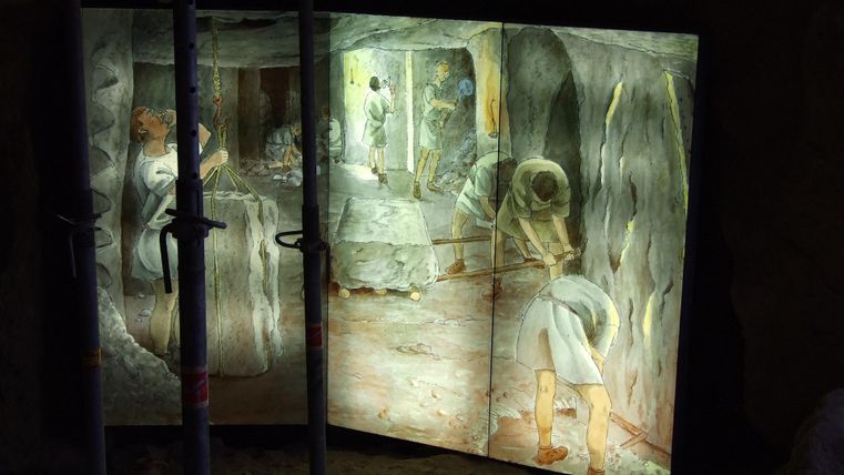 Eine künstlerische Darstellung von Arbeitern in einer Höhle, beleuchtet von hinten. Die Szenerie zeigt verschiedene Figuren, die mit Werkzeugen beschäftigt sind.