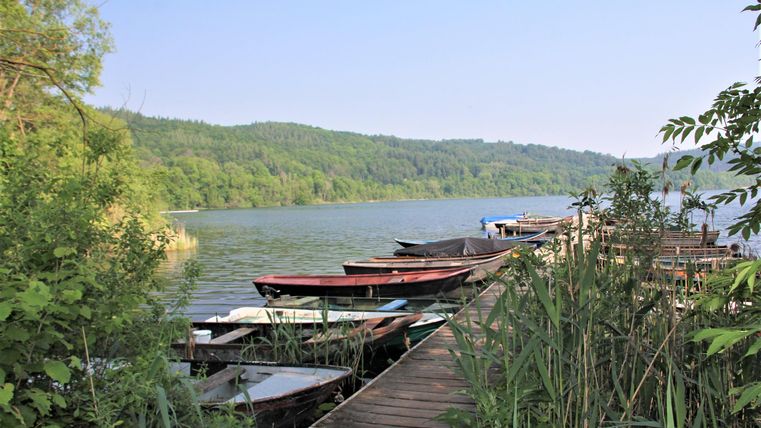 Ein ruhiger See mit mehreren Booten am Ufer. Die Umgebung ist grün und von Bäumen umgeben.