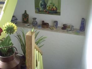 A small niche with decorative ceramics and a mural depicting fruit. Some plants and a pot are also nearby.