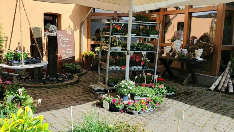 A blooming garden with colorful plants and flowers. In the background, decorative garden items and a cozy seating area can be seen.