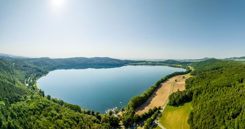 A beautiful lake surrounded by lush nature and forests. The clear water surface reflects the blue sky.