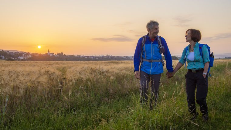 Ein Paar wandert bei Sonnenuntergang durch ein Feld, mit einer Stadt im Hintergrund.