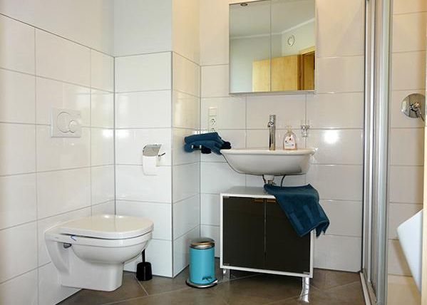 A modern bathroom with a WC, a sink, and a mirror. The walls are decorated with white tiles and there is a shower in the corner.